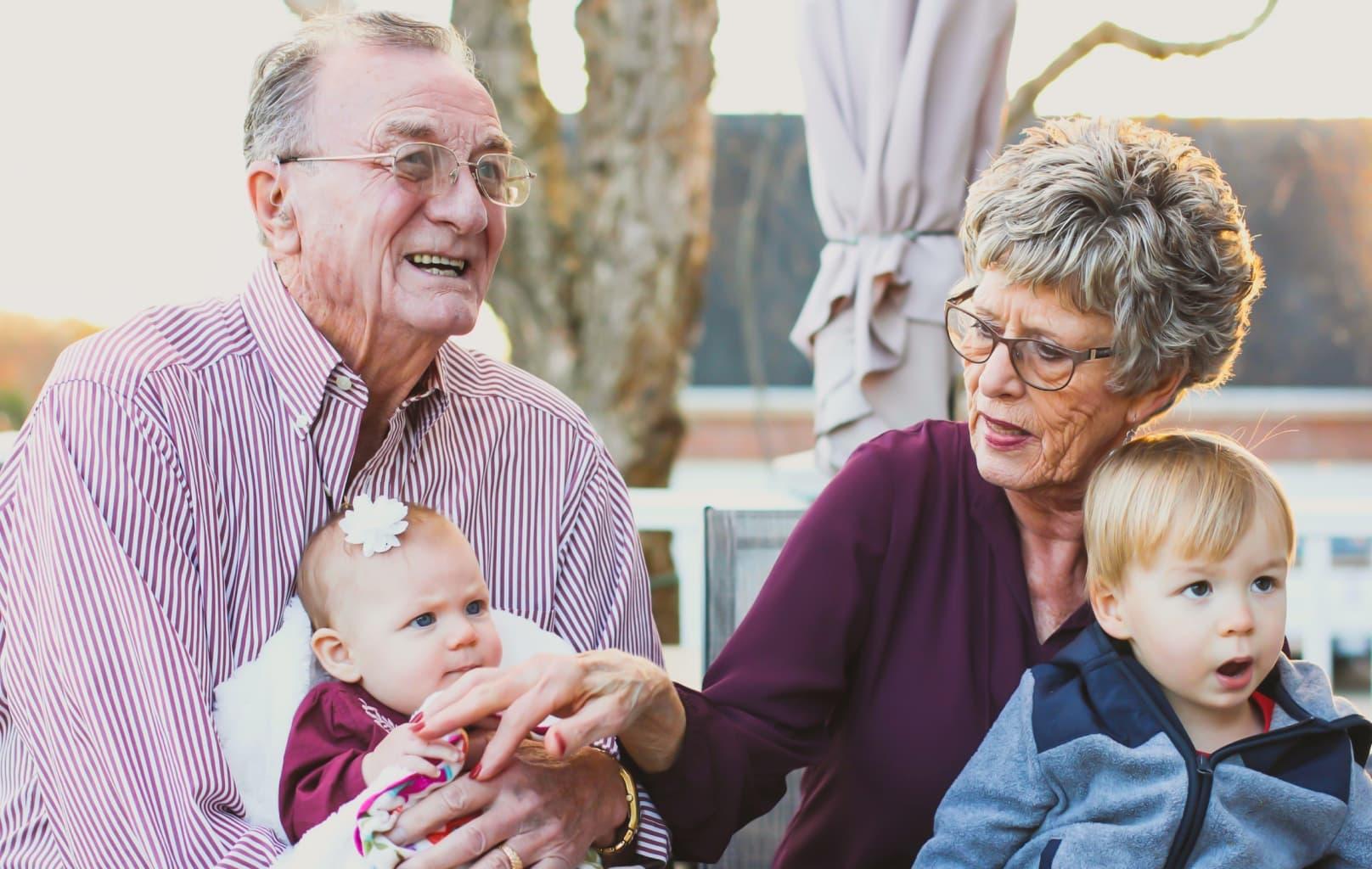 Elderly couple smiling and holding grandchildren